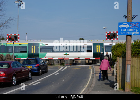 traffic building up with railway level crossing barriers down with a train speeding through Stock Photo