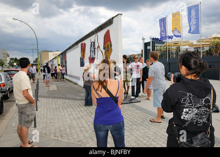 Eastside Gallery, young tourists at the painted, remaining part of the Berlin Wall in Friedrichshain district, Berlin, Germany. Stock Photo