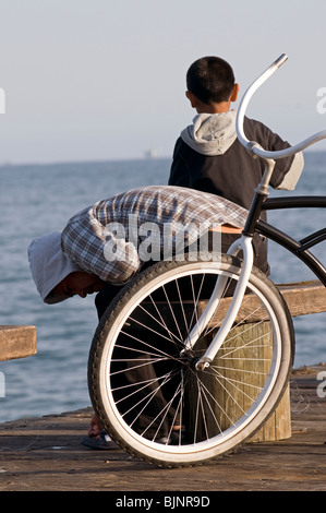 Two young men with hoodies sitting on bench pier near ocean Stock Photo
