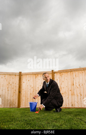 Businessman in front of a fence with a pail and shovel Stock Photo