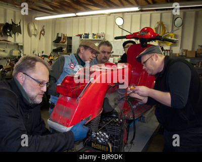 Scooter club members working on Vespa P200 repair and restoration in shop Stock Photo
