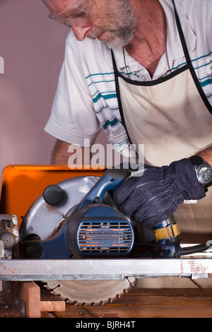 Carpenter using a bench mounted circular saw to cross cut a length of hardwood. Stock Photo