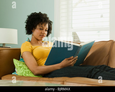 USA, Utah, Provo, young woman lying down on sofa and reading book Stock Photo