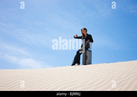 USA, Utah, Little Sahara, businesswoman sitting on suitcase in desert Stock Photo