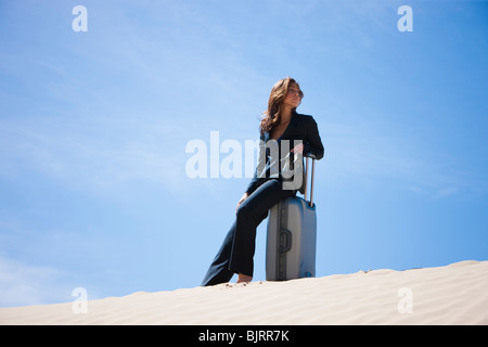 USA, Utah, Little Sahara, businesswoman sitting on suitcase in desert Stock Photo