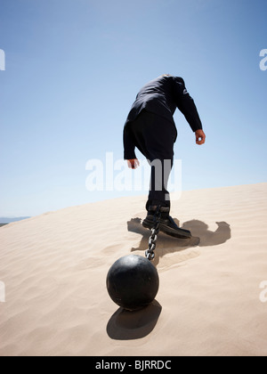 USA, Utah, Little Sahara, mid adult businessman pulling ball in chain on desert, rear view, low angle view Stock Photo