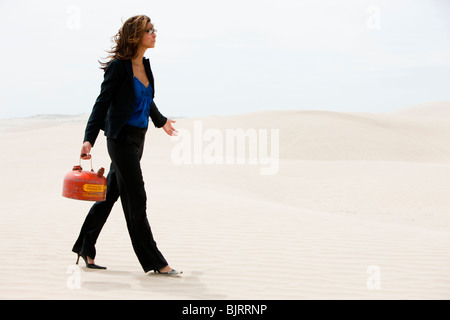 USA, Utah, Little Sahara, young businesswoman walking on desert carrying gas can Stock Photo