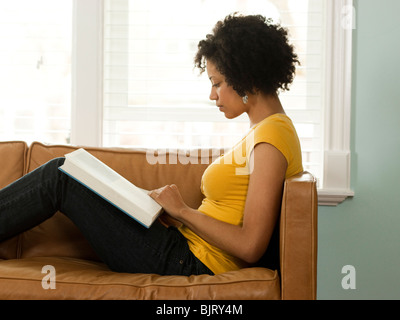 USA, Utah, Provo, young woman reading book on couch, side view