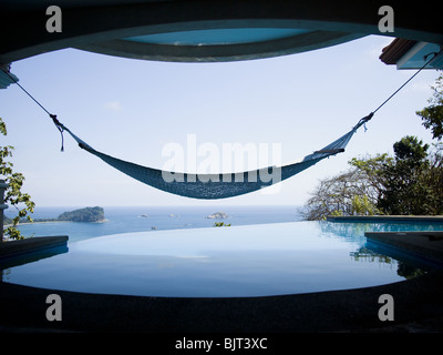 Man relaxing in a hammock overlooking infinity pool Stock Photo