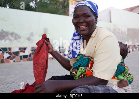 A mother carrying her baby sorts through clothes she is selling on the pavement. Benguela, Angola. Africa. © Zute Lightfoot Stock Photo