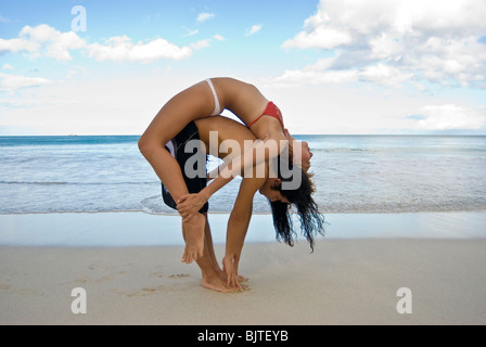 Young couple ( Asian man and Caucasian woman) in early twenties doing partner yoga on white sand beach in Hawaii Stock Photo