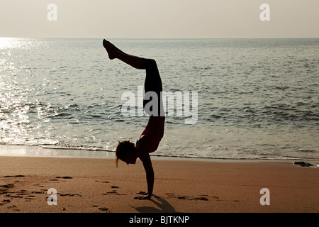 Woman practicing yoga on a beach at sunset Stock Photo