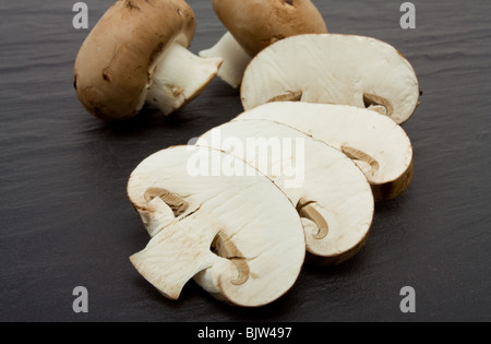 Sliced and whole Chestnut Mushrooms on background of dark slate. Stock Photo