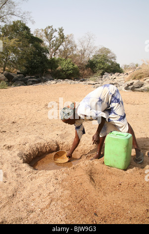 A blind African woman collects water from a dry river bed in Northern Ghana, West Africa Stock Photo