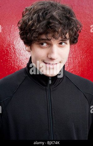 Portrait of young man smiling looking sideways with red background Stock Photo