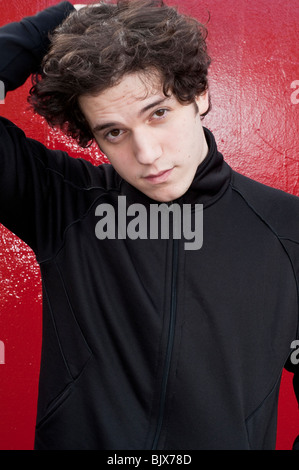 Portrait of young man running his fingers through his hair with red background Stock Photo