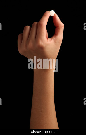 A female hand holding a small white pill between fingers Stock Photo