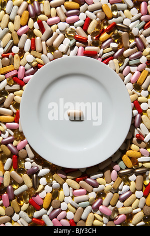 An empty white dinner plate with one pill on a background of colorful capsules, tablets and pills Stock Photo