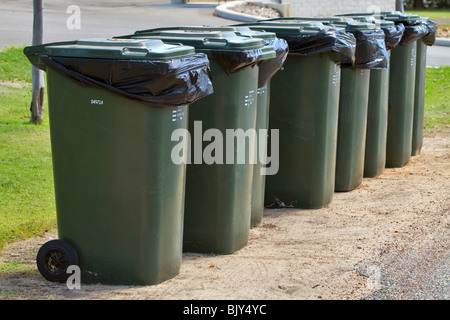 Row of wheelie bins waiting for pickup. Green bins for household refuse waiting beside the road. Stock Photo