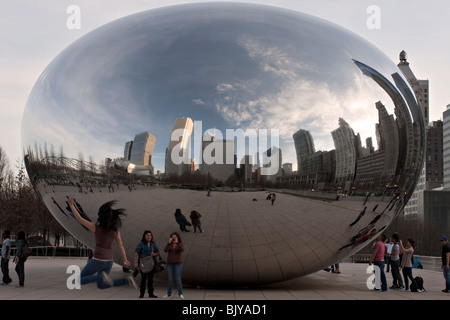 Excited visitors including a jumping girl at the AT&T plaza by the cloud gate sculpture reflecting Chicago skyline Stock Photo