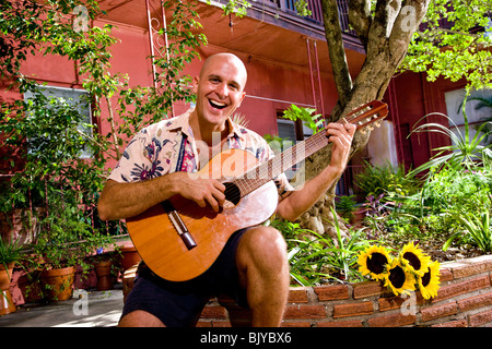 Portrait of smiling young man playing guitar in courtyard Stock Photo