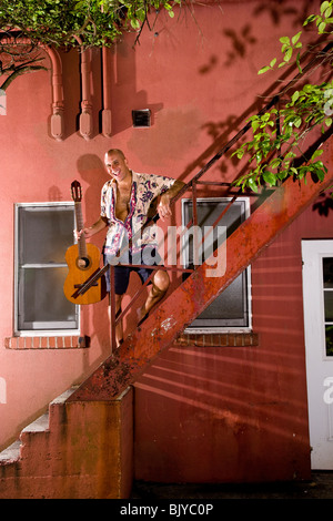Portrait of smiling young man holding guitar on staircase of red building Stock Photo