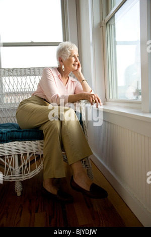 Portrait of smiling senior woman sitting on chair looking out window Stock Photo