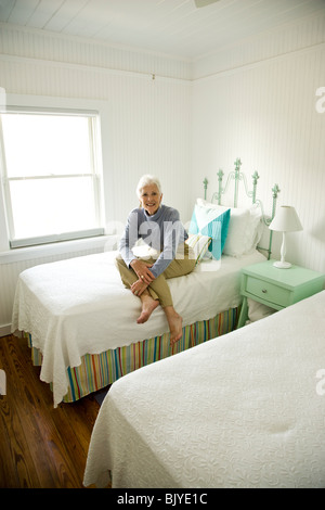 Senior woman sitting on bed in white bedroom Stock Photo