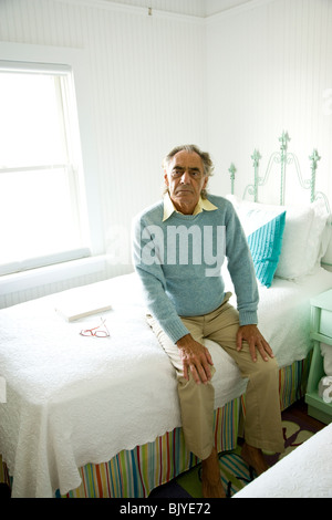 Portrait of serious senior man sitting on edge of bed Stock Photo