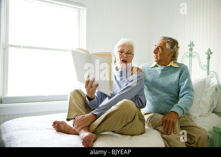 Senior couple sitting on bed reading book Stock Photo