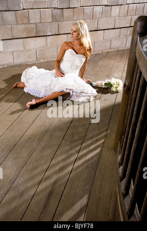 Young woman in white dress sitting barefoot on floor with bouquet Stock Photo