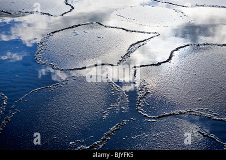 Thin ice breaking on a spring day, clouds and sky reflected in the water. Stock Photo