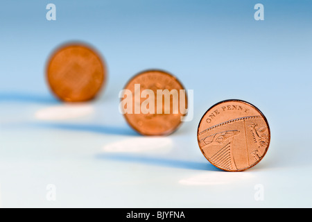 Three one penny pieces in diagonal line against a blue background with the 2nd and 3rd coins out of focus Stock Photo