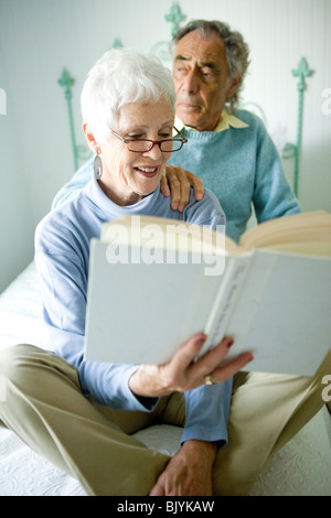 Senior couple sitting on bed reading book Stock Photo