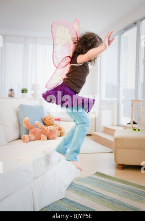 Hispanic girl in fairy wings jumping off couch Stock Photo