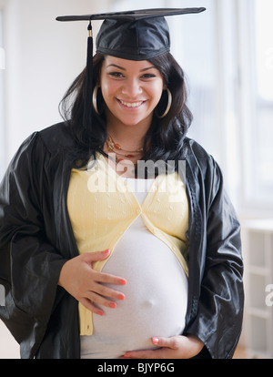 Pregnant Hispanic woman in graduation cap and gown Stock Photo