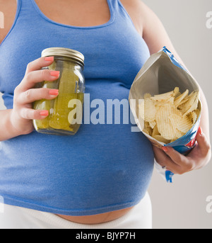 Pregnant Hispanic woman holding pickles and potato chips Stock Photo