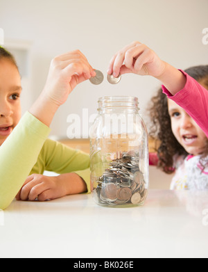 Hispanic sisters putting coins in jar Stock Photo