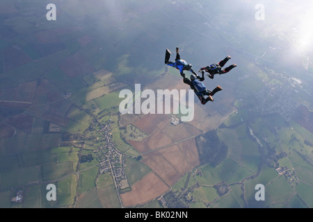 Three skydivers in free fall with the sun lightning up the earth below