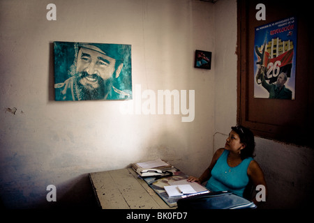 A Cuban office worker watching a painted portrait of the Cuban Revolutionary leader Fidel Castro in Santiago de Cuba, Cuba. Stock Photo