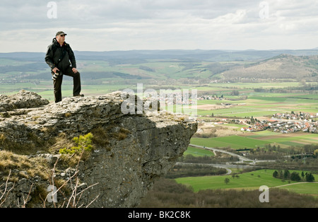 Man with camera on rocky outcrop on Staffelberg hill, overlooking river Main Valley, Staffelstein, Franconia, Bavaria, Germany. Stock Photo