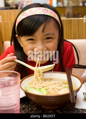 Chinese girl eating shrimp wonton and noodle soup with spoon and chopsticks at Chi Cafe in Chicago, IL Stock Photo