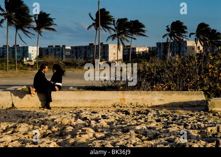 Cuban lovers sitting and embracing on the ruins of a devastated sea promenade during the sunset in Alamar, Havana, Cuba. Stock Photo