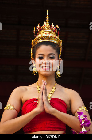 Young Thai woman in traditional costume and hands together in 'wai' greeting pose; at Siam Niramit; Bangkok, Thailand. Stock Photo