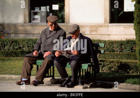 Two elderly men sitting on a bench in Portugal - One man is reading a magazine Stock Photo