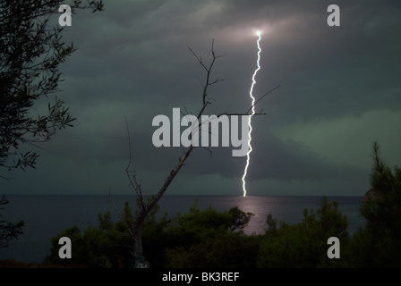 A lightning bolt hits the sea in contrast to a dried up olive branch reaching for the night sky during a summer storm. Thassos, Greece. Stock Photo