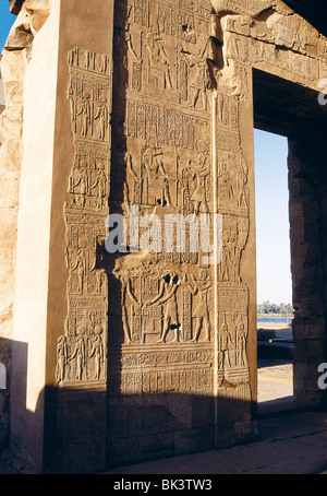 Architectural detail of ancient temple ruins with bas-relief sculpture depicting Egyptian deities and hieroglyphics in Egypt.