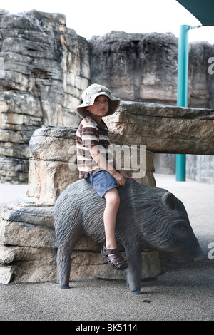 Boy Sitting on Statue of Boar Stock Photo