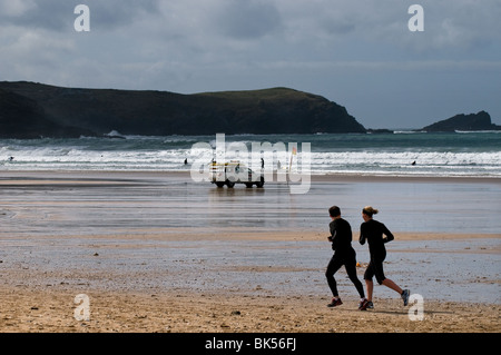 Two people running past a RNLI patrol vehicle on Fistral Beach in Newquay in Cornwall.  Photo by Gordon Scammell Stock Photo