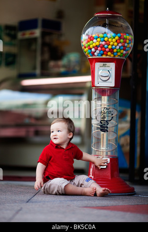 Young boy sitting by large gumball machine